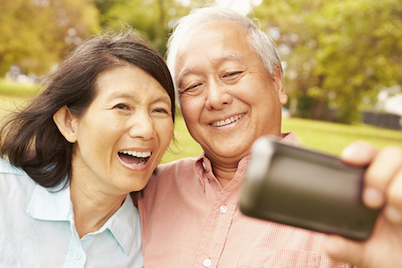 Asian couple smiling for a selfie with bright white smiles resulting from cosmetic dentistry services like teeth whitening. 